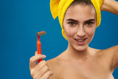 Portrait of young woman smiling while holding razor against blue background