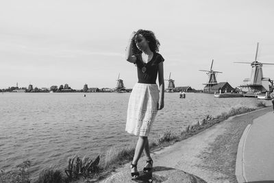 Young woman standing by river against sky