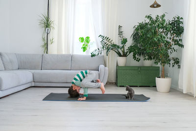 Cat sitting by boy exercising on mat at home