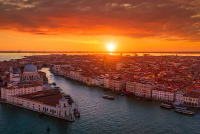 Scenic view of river by buildings against sky during sunset