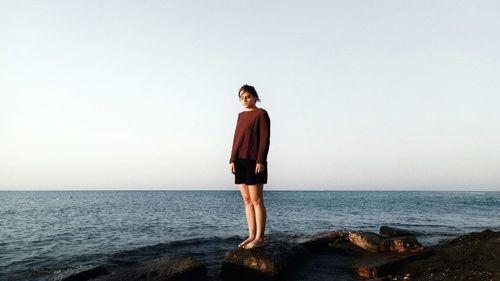 Young woman standing in front of sea against clear sky