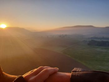 Midsection of person on mountain against sky during sunset