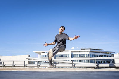 Man jumping in city against blue sky