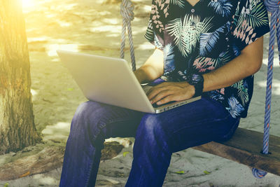 Midsection of man using mobile phone while sitting on tree