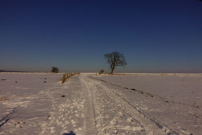 Scenic view of snow covered land against clear blue sky during winter