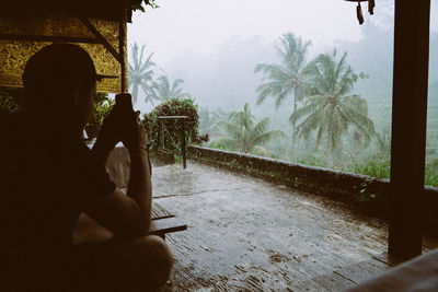 Man using mobile phone against trees during rainy season