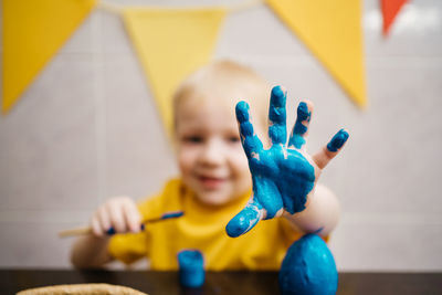 Little boy draws blue paint on his hand, paints an easter egg