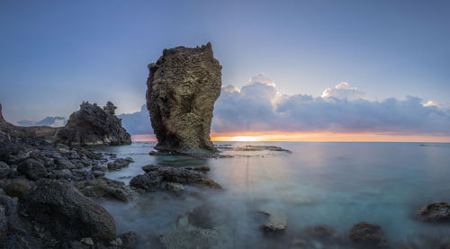 Rock formation on beach against sky during sunset