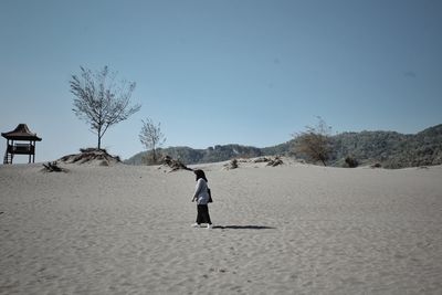 Woman walking on sand against blue sky at beach