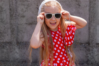 Beautiful happy girl in red polka dot dress smiling concrete wall background. cute  child long hair