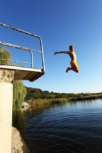Man jumping over lake against clear sky