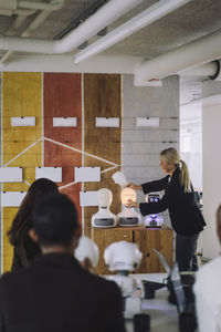 Mature female professor discussing with students over social robot in innovation lab