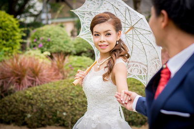 Smiling young bride holding groom hand in park