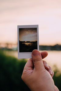 Close-up of hand holding instant print transfer against sky