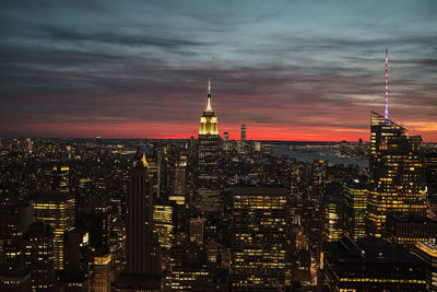 Illuminated buildings in city against cloudy sky