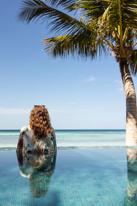 Relaxed woman into a infinity swimming pool looking the ocean