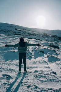 Rear view of man with arms stretched standing on snow covered land