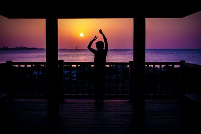 Silhouette woman standing by sea against sky during sunset