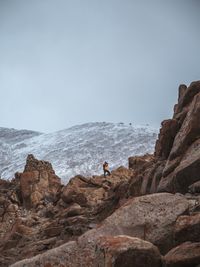 Mid distance of male hiker standing on rocky mountain against clear sky