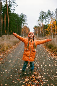 Girl in orange coat with outstretched arms enjoys fresh air in fall forest. mental health, autumn
