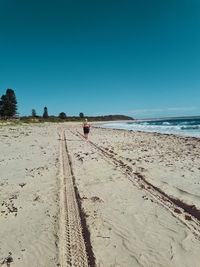 Rear view of woman running at sandy beach against blue sky