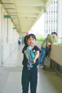 Portrait of girl holding toy while standing in corridor