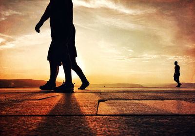 Silhouette men walking on beach against sky during sunset