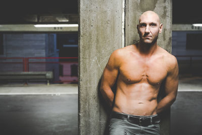 Shirtless muscular man leaning on wall in parking lot