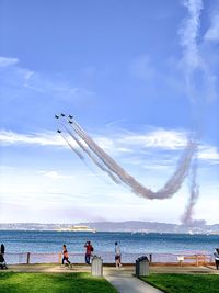 People at airplane by sea against sky