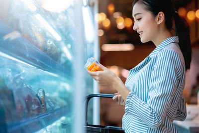 Side view of young woman holding ice cream at store