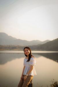 Portrait of young woman standing in lake against sky