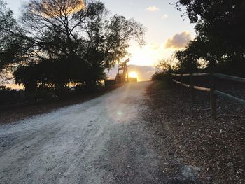 Road amidst trees against sky during sunset