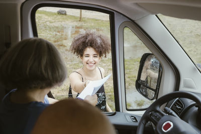 Happy young woman with map helping senior couple in camper van