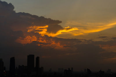 Silhouette of city against cloudy sky during sunset