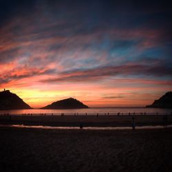 Scenic view of beach against dramatic sky during sunset