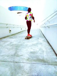 Rear view full length of woman skateboarding on footbridge