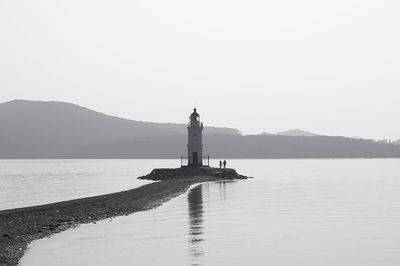 Lighthouse by sea against clear sky