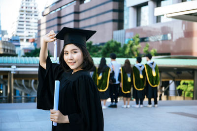 Young woman wearing black graduation gown standing in city