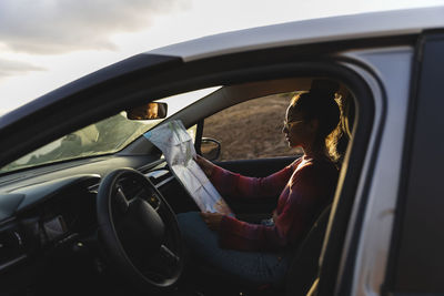 Young woman checking map in car at sunset