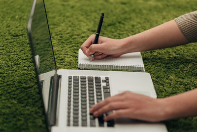 Midsection of woman writing in diary while using laptop on grass