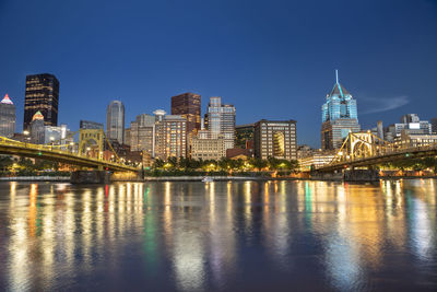 Illuminated buildings by river against sky in city