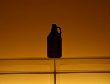 Close-up of orange bottle on table against wall