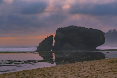 Rocks on beach against sky during sunset