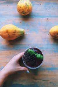 Cropped image of hand holding flower pot on table with papayas