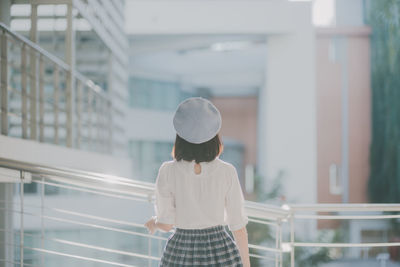 Rear view of young woman standing on footbridge by railing in city