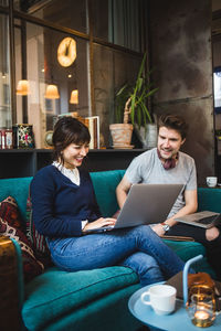 Smiling multi-ethnic male and female entrepreneurs discussing over laptop on sofa at office