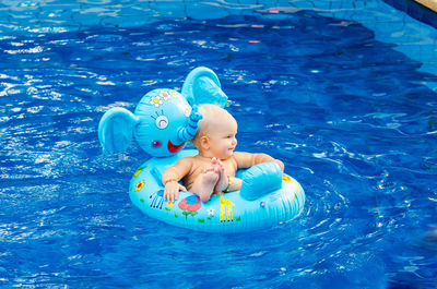 High angle view of shirtless girl sitting in inflatable ring on swimming pool