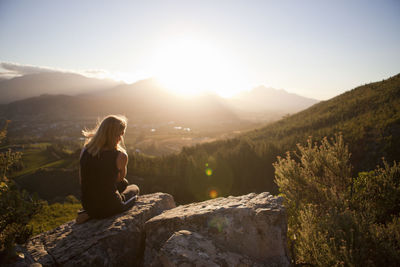 Woman sitting on mountain and looking at sunset