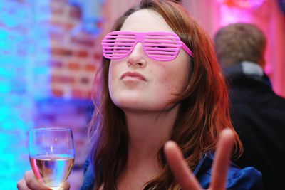 Portrait of young woman wearing pink eyeglasses gesturing peace sign