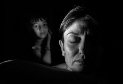 Close-up of mother with eyes closed against daughter in darkroom